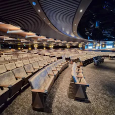 Empty curved auditorium with rows of upholstered seats, overhead lights and stage rigging