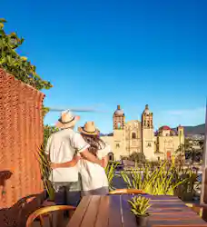 Couple in straw hats embracing on rooftop terrace overlooking ornate cathedral and blue sky