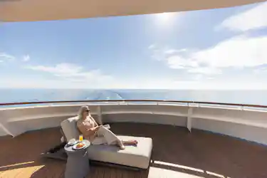 Woman wearing sunglasses reading on cruise deck lounge chair beside breakfast, ocean horizon