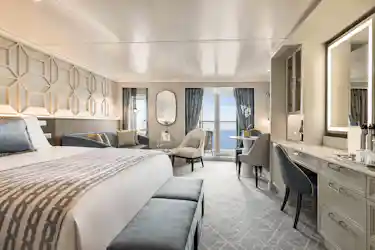 Luxurious bedroom with king bed, seating area, desk and balcony overlooking the ocean
