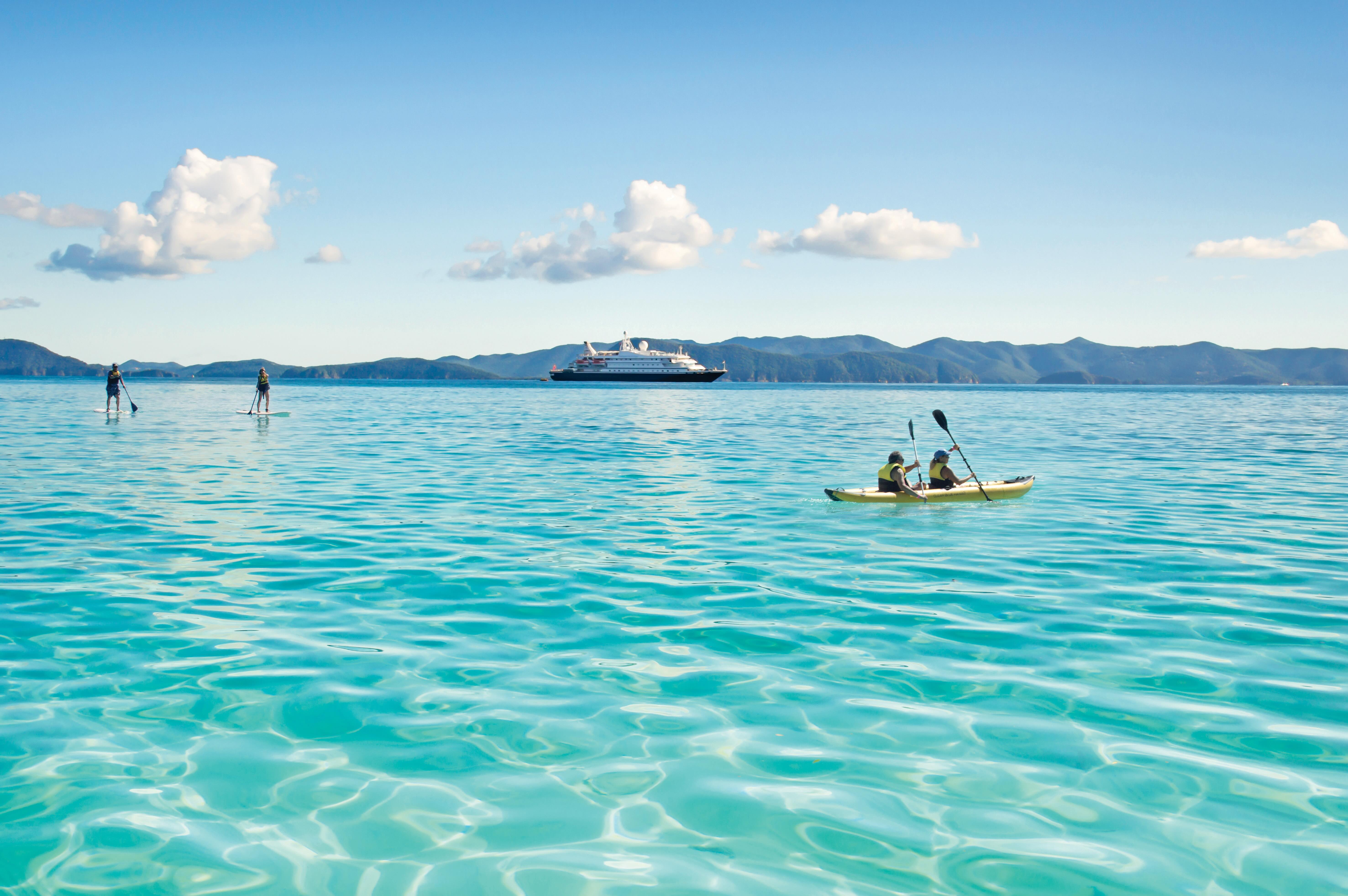 Two kayakers paddling turquoise sea with two paddleboarders and cruise ship near islands
