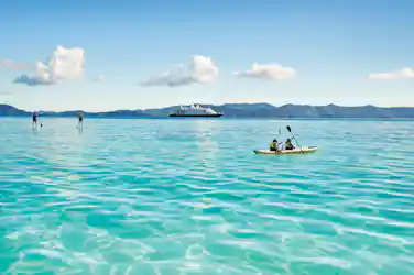 Two kayakers paddling turquoise sea with two paddleboarders and cruise ship near islands