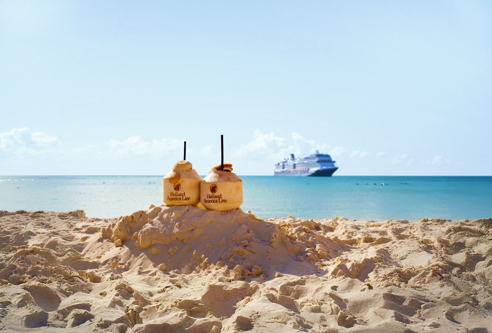 Two Holland America Line coconuts with straws on a sandy beach, cruise ship on the horizon.