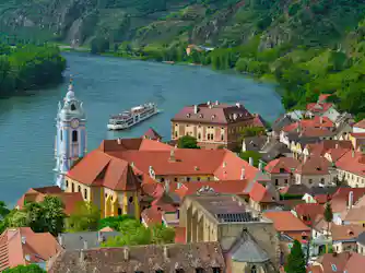 River cruise ship passing a baroque blue church tower beside red-roofed town and green hills