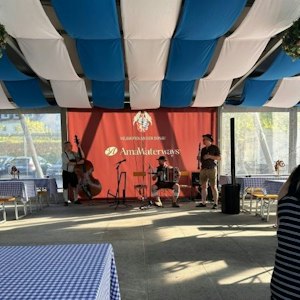 Three musicians (double bass, accordion, clarinet) on AmaWaterways stage under blue-white canopy