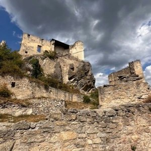Ruined medieval stone castle perched on a rocky hill with terraced walls beneath stormy clouds