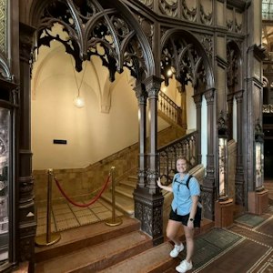 Visitor in blue shirt by ornate Gothic wooden arch and roped staircase in historic interior