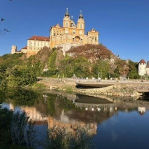 Baroque yellow abbey with twin towers on a rocky hill, reflected in calm river