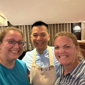 Three-person selfie: two women and a male chef in apron with name tag in a dining room