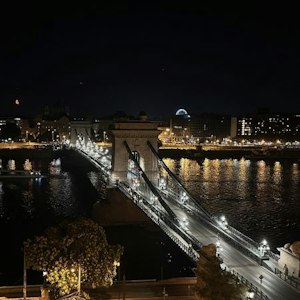 Illuminated Chain Bridge across the Danube at night with city lights, reflections, and crescent moon