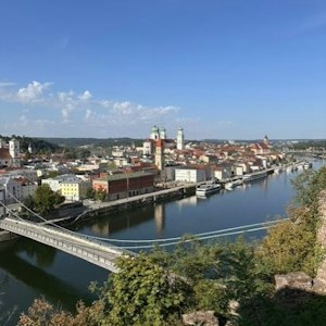 Panoramic riverside European town with a suspension bridge and twin green‑domed cathedral.u
