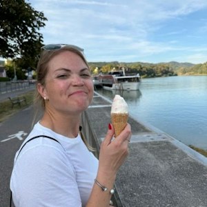 Smiling woman in white shirt holding ice cream cone on river promenade with docked boats