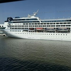 Large white multi-deck cruise ship docked at pier with orange lifeboats, calm water