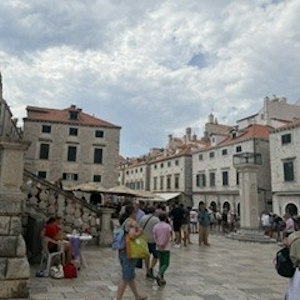 Historic stone town square with red‑roofed buildings, tourists walking and sitting