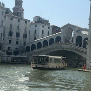 Vaporetto waterbus passing under Venice's Rialto Bridge on the Grand Canal with historic buildings.