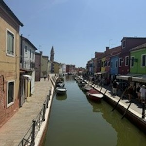 Canal flanked by colorful houses and boats, pedestrian walkways and distant bell tower