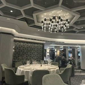 Upscale dining room with round set table, chairs, patterned wall and geometric ceiling chandelier