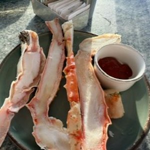 Split crab legs served on a plate with a small cup of red dipping sauce and napkins.