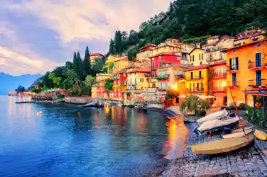Colorful lakeside village on hillside with moored boats, cobbled shore and mountain backdrop