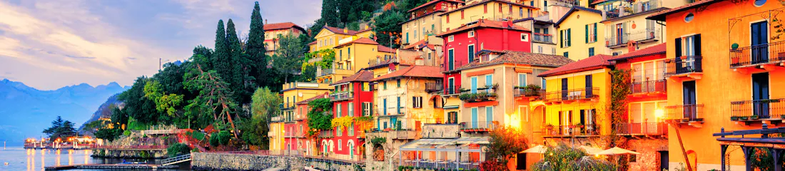 Colorful lakeside village on hillside with moored boats, cobbled shore and mountain backdrop