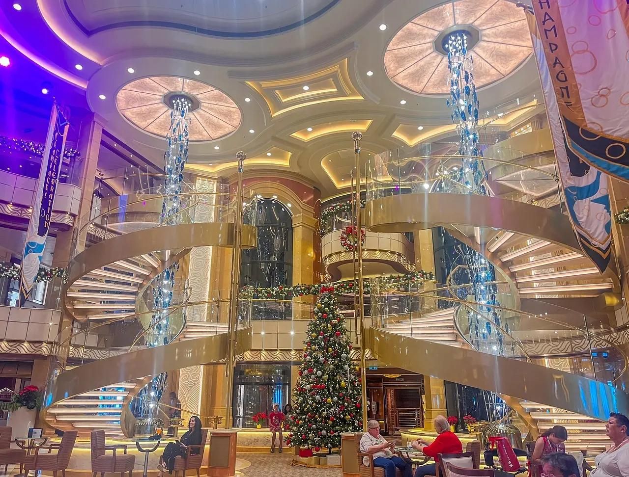 Grand atrium with double spiral staircases, tall glass chandeliers and decorated Christmas tree.