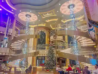Grand atrium with double spiral staircases, tall glass chandeliers and decorated Christmas tree.