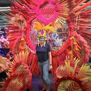 Woman in yellow feathered headdress poses before red-orange circular carnival feather display