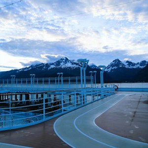 Cruise ship deck with curved running track, railings and lights facing snow‑capped mountains