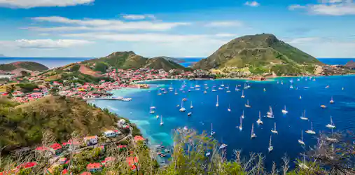 Panoramic harbor with turquoise water, dozens of sailboats and red-roofed hillside village