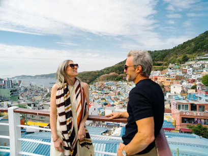 Couple in sunglasses laughing on rooftop overlooking colorful hillside coastal town and harbor