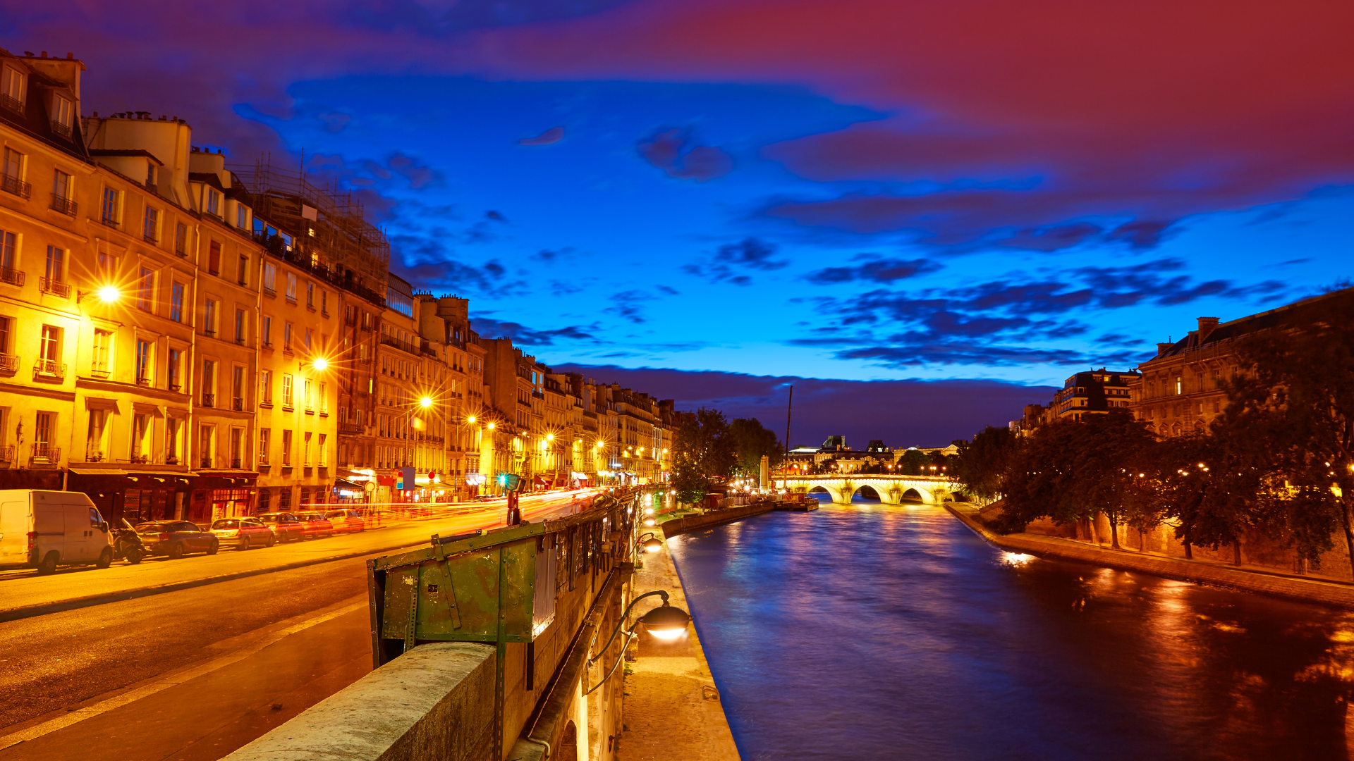 Paris riverside at dusk with illuminated Haussmann buildings and arched bridge over the Seine