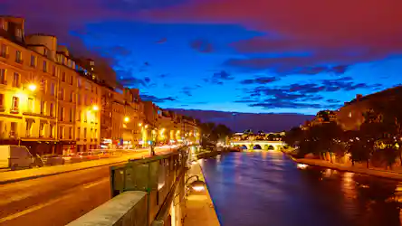 Paris riverside at dusk with illuminated Haussmann buildings and arched bridge over the Seine