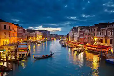 Venice Grand Canal at dusk with gondolas, lit waterfront buildings and reflections