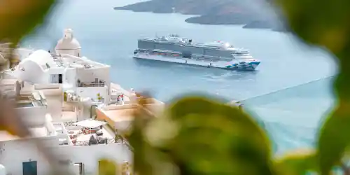 White Cycladic buildings and dome overlooking a cruise ship in blue caldera waters