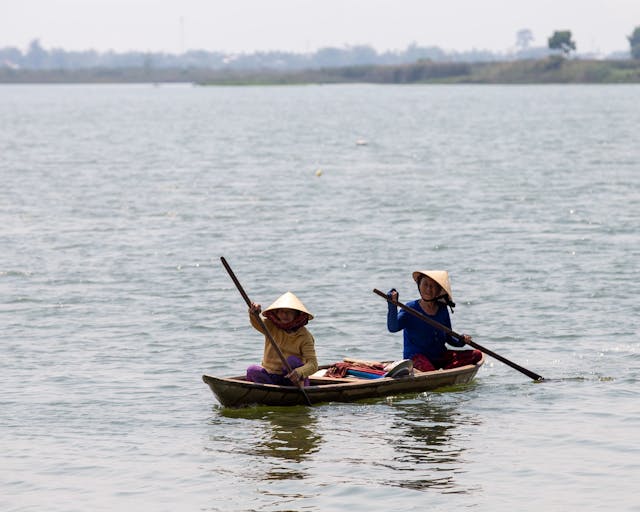 Two people in traditional clothing in a canoe in a lake.