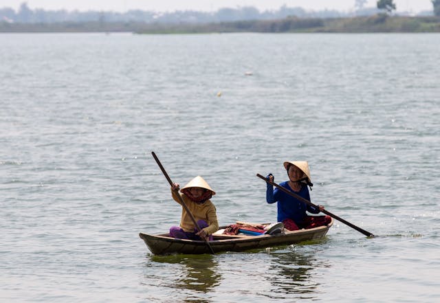 Two people in traditional clothing in a canoe in a lake.