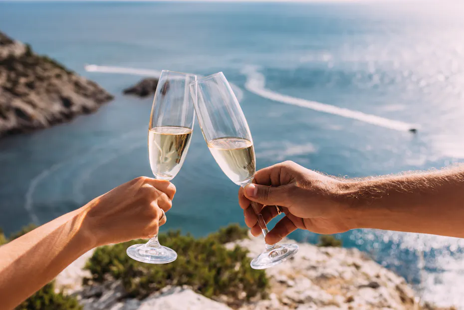 2 people clinking champagne glasses together overlooking ocean