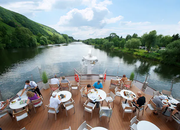 Ship deck with people eating at tables and river in background