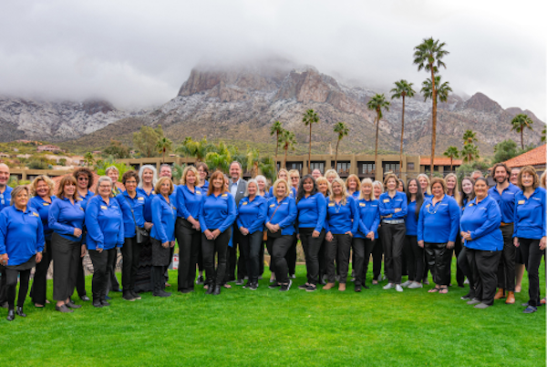 team of insiders with blue collared shirts in front of a beautiful mountain with clouds sitting on top